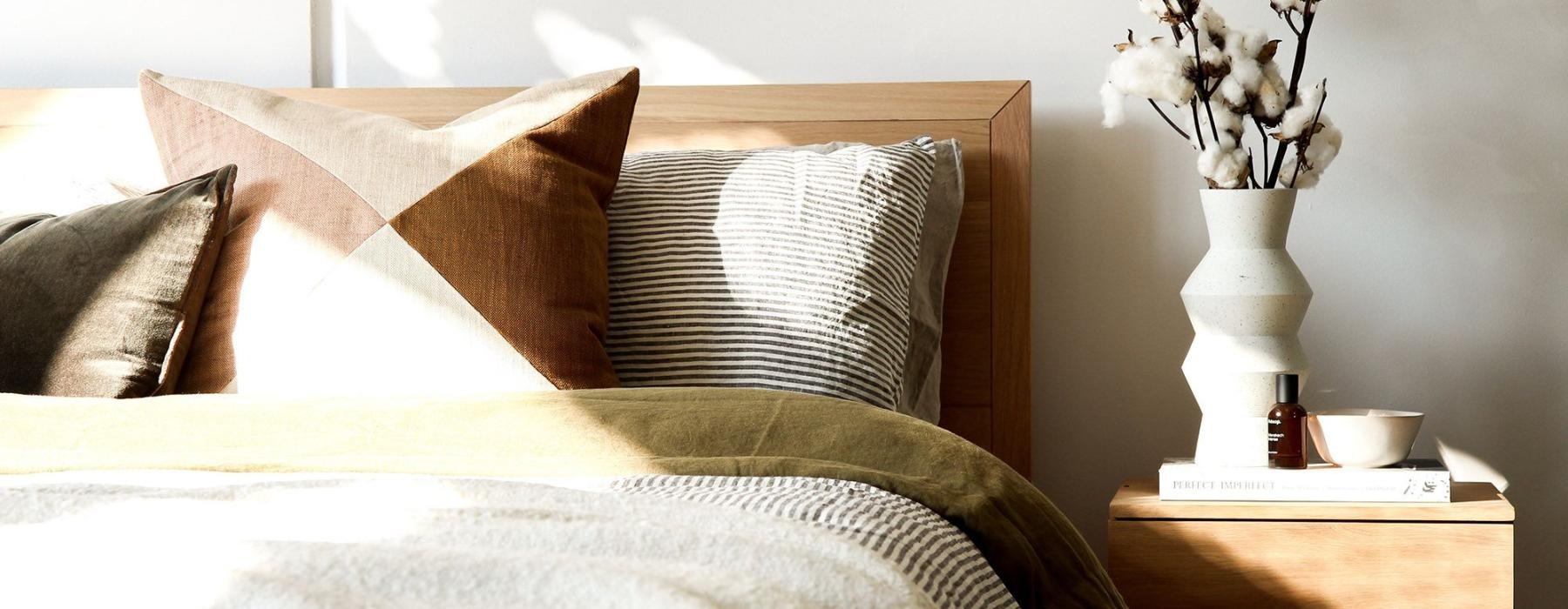 swath of sunlight shines across a well made bed and bedside table with a vase of cotton plants